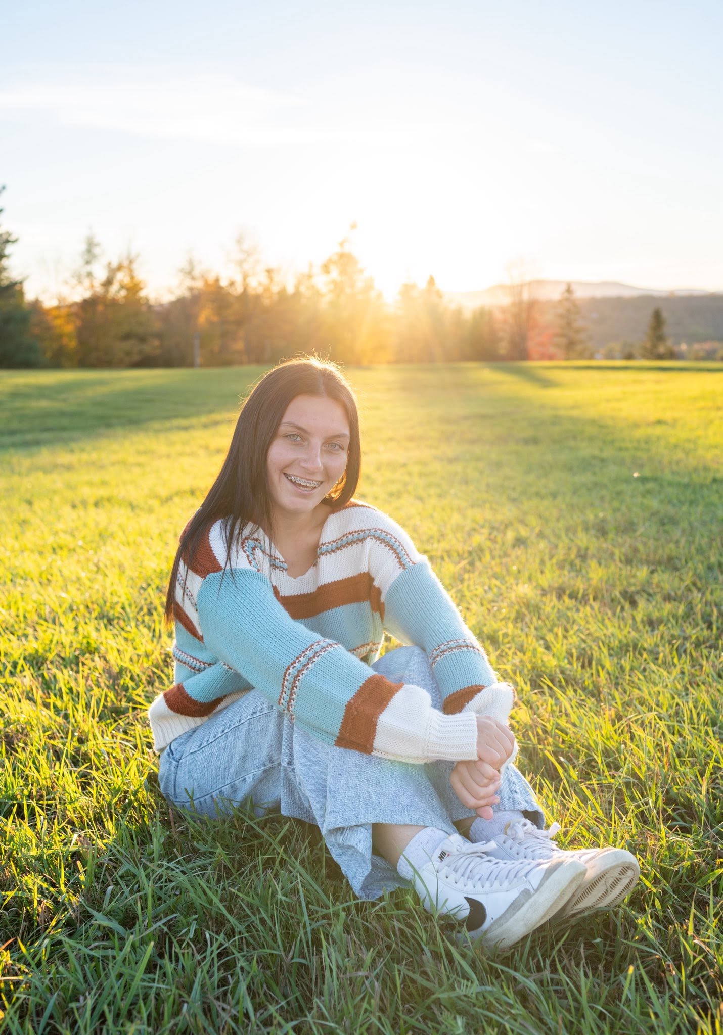 A high school senior standing outdoors among tall grasses during a fall senior portrait session.